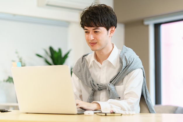 Asiatischer junger Mann mit einem Laptop in einem ungezwungenen Zimmer