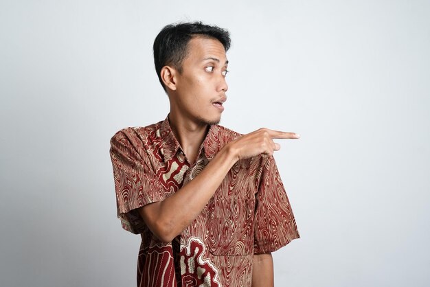 Foto asiatischer junger mann mit gebräunter haut, der ein batikhemd trägt, das auf den leeren raum der seite für werbung zeigt, braucht weißen hintergrund