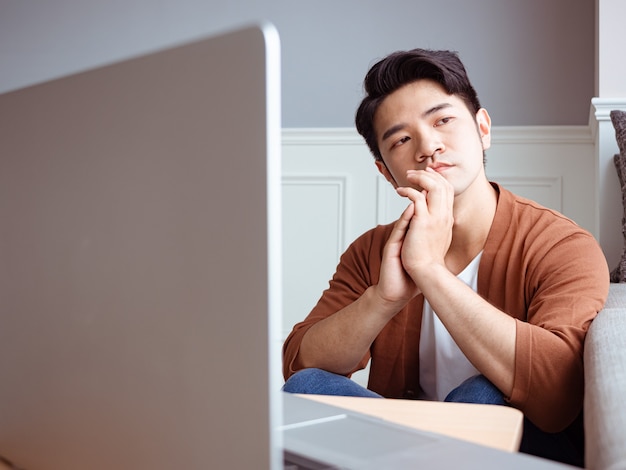 Asiatischer junger Mann sitzt am Tisch vor Laptop-Computer