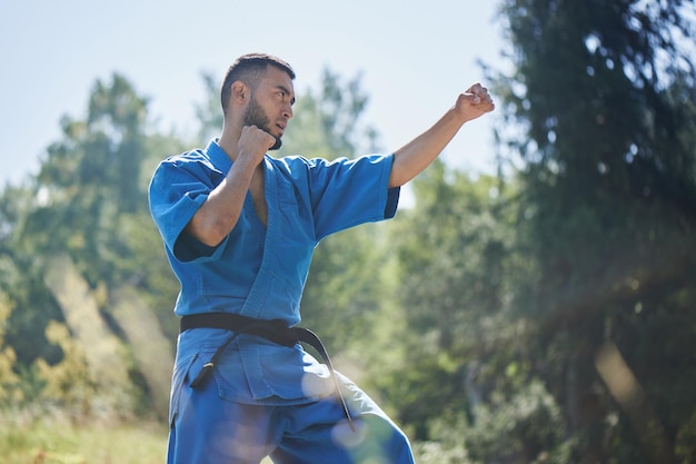 Asiatischer kasachischer Karate-Kämpfer kämpft in blauer Kimono-Uniform auf einer sommerlich schönen Naturlandschaft mit Kopierraum