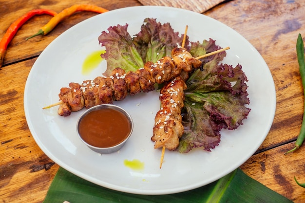 Asiatischer Kebab im tropischen Stil auf dem Teller mit Bananen- und Salatblättern und Sesamsamen auf Holztisch