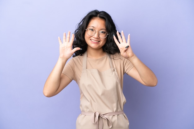 Asiatischer Kellner im Restaurant isoliert auf violettem Hintergrund, der neun mit den Fingern zählt