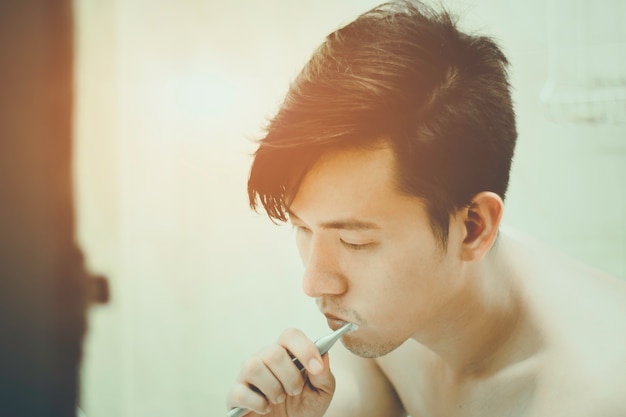 Asiatischer Kerl putzt seine Zähne im Badezimmer