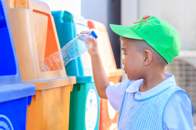 Asiatischer Kinderjunge, der eine Plastikflasche in einen Papierkorb wirft. Umweltkonzept speichern.