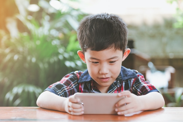 Asiatischer kleiner Junge, der Online-Spiel spielend sitzt