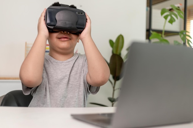 Asiatischer kleiner Junge mit VR-Brille, der zu Hause Wissenschaften studiert