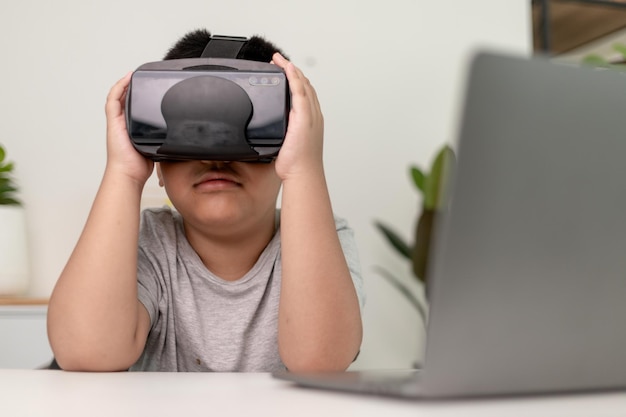 Asiatischer kleiner Junge mit VR-Brille, der zu Hause Wissenschaften studiert