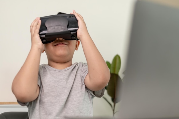 Asiatischer kleiner Junge mit VR-Brille, der zu Hause Wissenschaften studiert