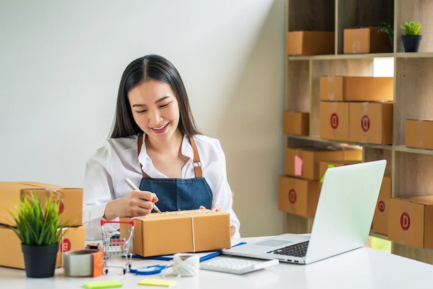 Asiatischer Kleinunternehmer hält einen Stift, um Adressen aufzuschreiben, um Pakete an Kunden Online-Verkauf mit Paketbox zu Hause zu liefern.