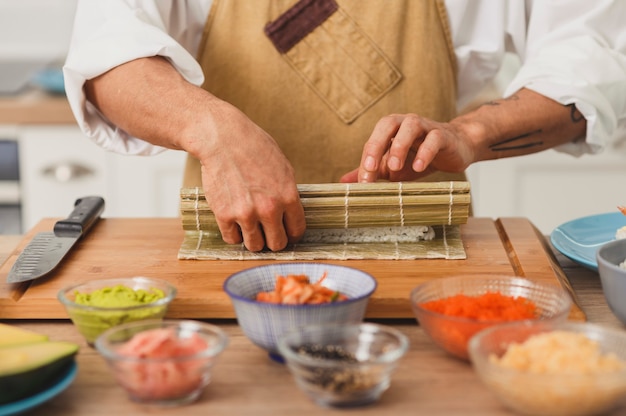 Asiatischer Koch übergibt rollendes Sushi mit Bambusmatten-Sushi-Vorbereitungsprozess mit Zutaten japanisches Essen