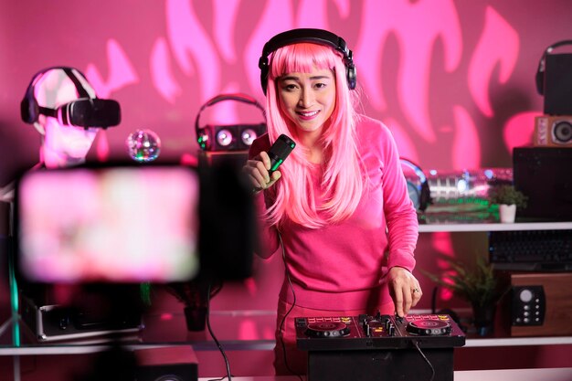 Asiatischer Künstler, der Techno-Songs am Mischpult spielt, während er mit einer professionellen Kamera eine Musiksession aufzeichnet und sich auf einen Auftritt im Nachtclub vorbereitet. Dj mit rosa Haaren mit Audiogeräten