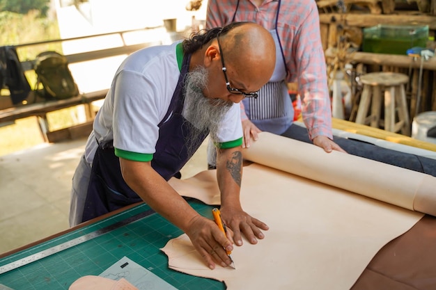 Asiatischer Lederhandwerker verwendet ein Schneidemesser, um ein Stück weißes Leder großes Blatt gemäß dem Design zu schneiden, um es in Produkte für Kunden zu nähen