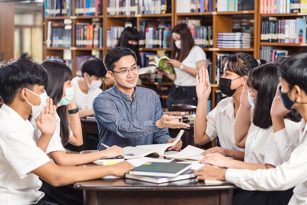 Asiatischer Lehrer hebt die Hand und gibt einer Gruppe von Studenten Unterricht