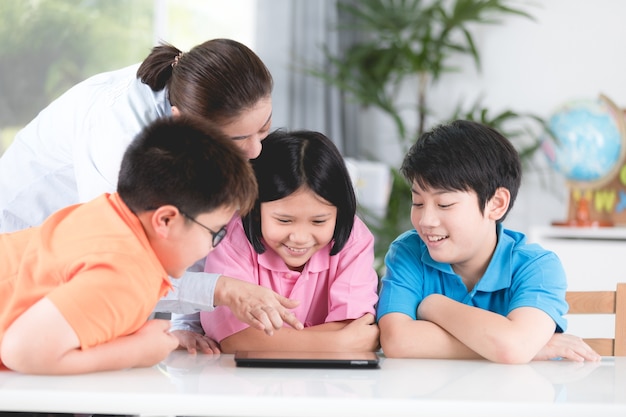 Asiatischer Lehrer und Kinder, die unter Verwendung der digitalen Tablette sich unterhalten