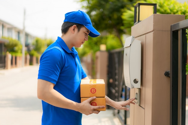 Asiatischer Lieferung junger Mann in der blauen Uniform, die eine Box hält