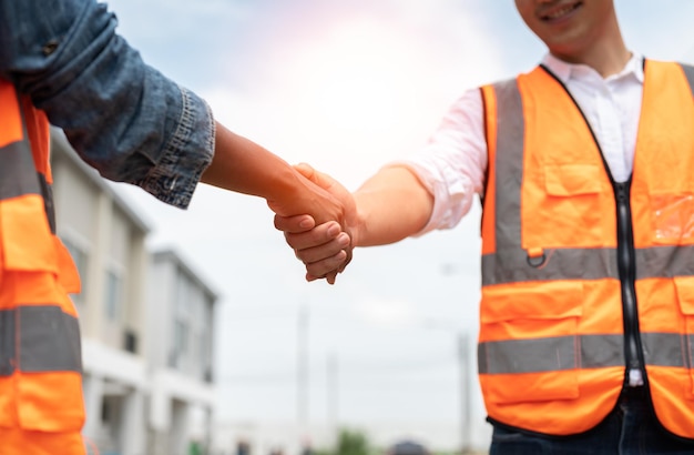 Asiatischer männlicher Ingenieur, der sich auf der Baustelle die Hände schüttelt, um ein Wohnsiedlungsprojekt zu vereinbaren