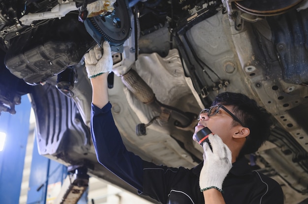 Asiatischer männlicher mechanischer Griff und glänzende Taschenlampe, zum des Autos unter Fahrgestellen zu überprüfen