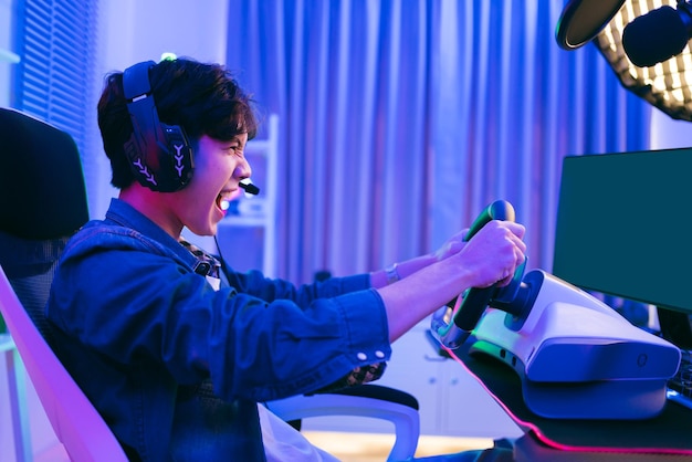 Asiatischer männlicher Pro-Gamer, der ein Online-Simulationsspiel für Autofahrten mit Lenkrad-Controller spielt Gamer, der ein Sportspiel mit Siegesgefühl gewinnt Der Spieler freut sich über den Sieg im Wettbewerb