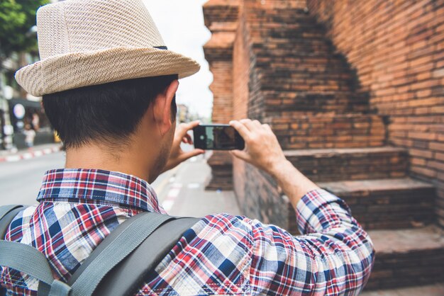 Asiatischer männlicher touristischer Wanderer, der Foto mit Smartphone bei Tha Phae Gate, einer des alten berühmten Marksteins der Stadt in Chiang Mai Thailand macht