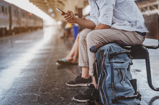 Asiatischer Mann, der am Bahnhof die richtige Richtung sucht. Reisender wartet auf den Zug und plant Ferien mit Smartphone. Urlaub, Reise, Reise und Sommer Reisekonzept.