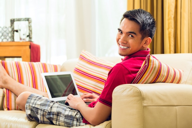 Asiatischer Mann, der auf der Couch surft das Internet sitzt