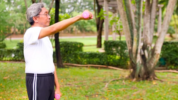 Asiatischer Mann, der Übung durch Anheben der Hanteln am Park tut.