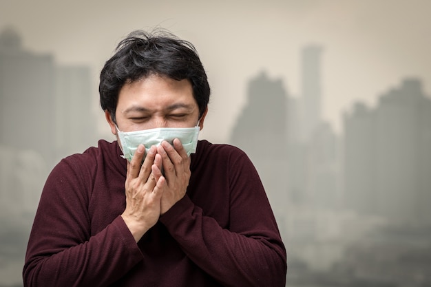 Asiatischer Mann, der die Gesichtsmaske gegen Luftverschmutzung mit dem Husten trägt