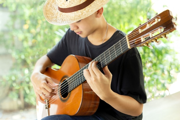 Asiatischer Mann, der eine klassische Gitarre in der Natur spielt.