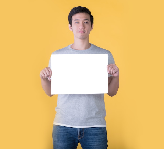 Asiatischer Mann, der eine leere Plakatwand auf gelbem Hintergrund hält