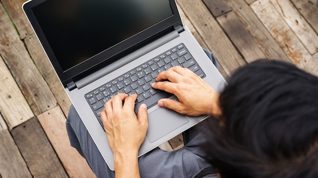 Asiatischer Mann, der einen Laptop auf dem Balkon verwendet.