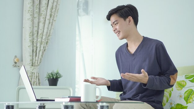 Asiatischer Mann, der glücklich von zu Hause mit Laptop arbeitet