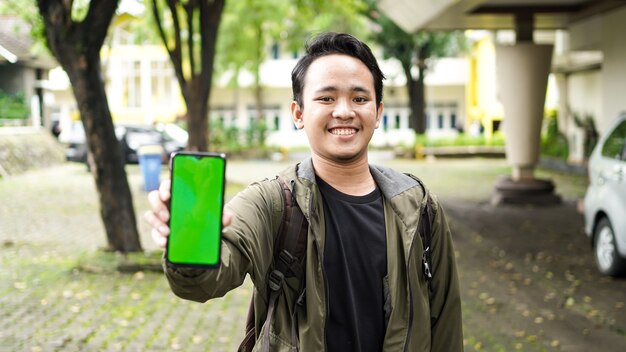 Asiatischer Mann, der grünes Bildschirmhandy trägt