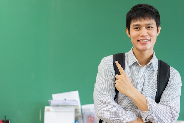 asiatischer Mann der jungen Highschool, der mit glücklichem Ausdruck lächelt und überreicht grünen Tafelhintergrund zeigt