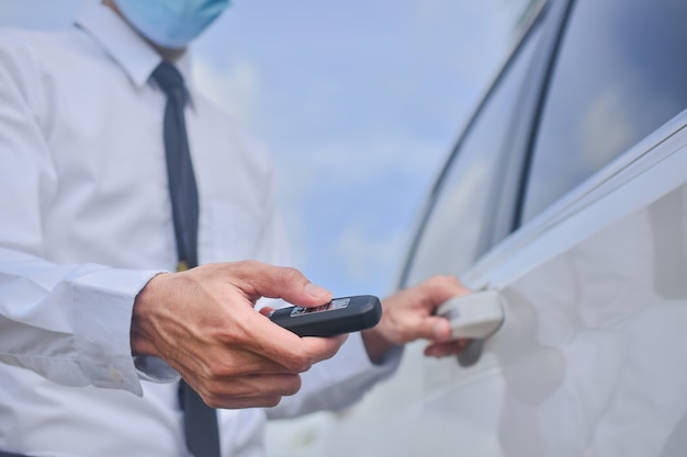 Asiatischer Mann, der medizinische Maske trägt und Schlüssel zum Öffnen der Autotür hält