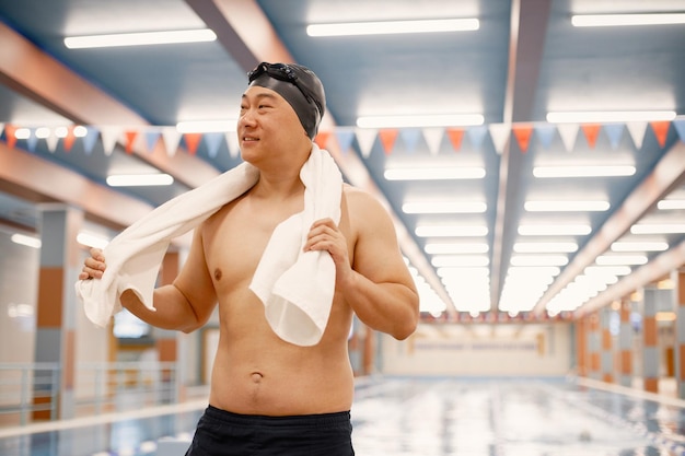 Asiatischer Mann, der mit einem Handtuch auf den Schultern im Innenpool steht