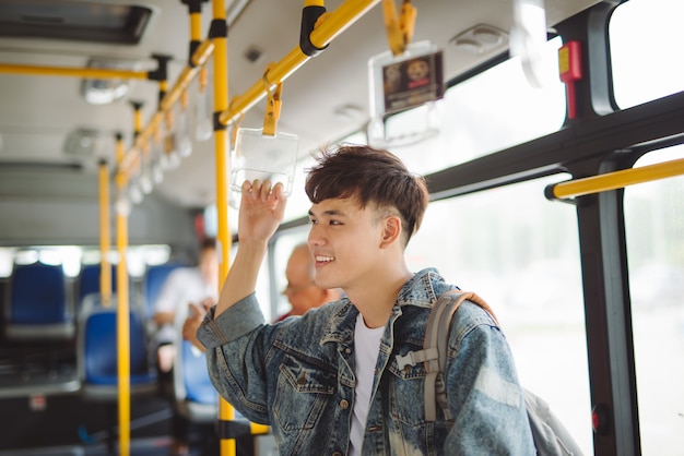 Asiatischer Mann, der öffentliche Verkehrsmittel nimmt und im Bus steht.