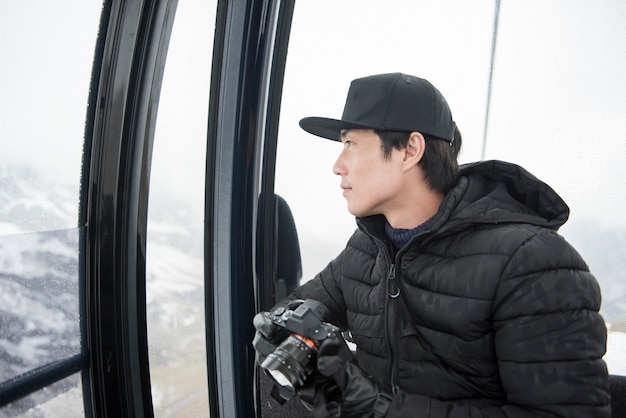 Asiatischer Mann, der seine Kamera verwendet, während Sie in der Drahtseilbahn sitzen