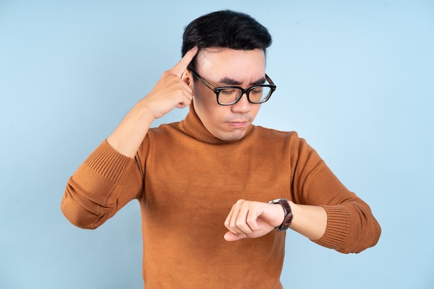 Asiatischer Mann, der seine Uhr auf blauem Hintergrund schaut