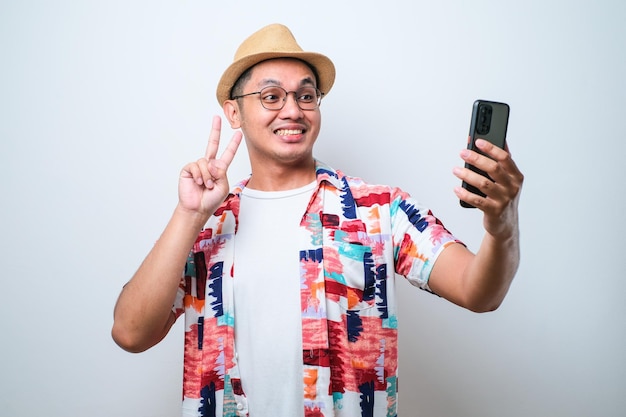 Asiatischer Mann, der Selfie-Foto auf Smartphone mit positivem Ausdruck mit Friedenshandgeste macht