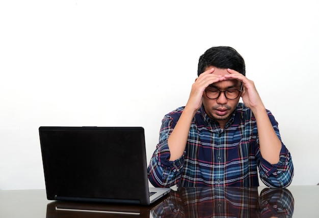 Asiatischer Mann, der träge nach unten schaut, wenn er neben seinem Laptop sitzt