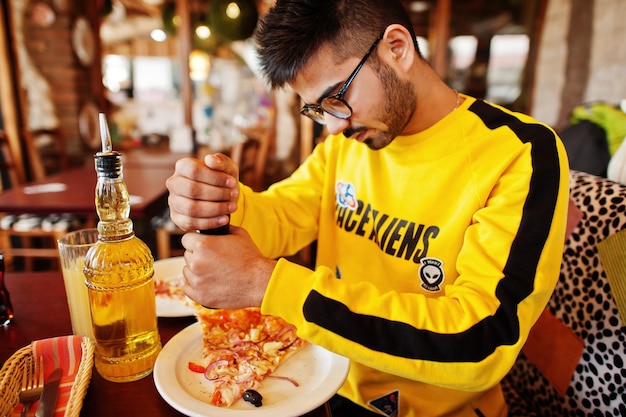 Asiatischer Mann, der während einer Party in der Pizzeria Pizza isst Typ, der italienisches Essen isst und auf der Couch sitzt und Pfeffer gießt