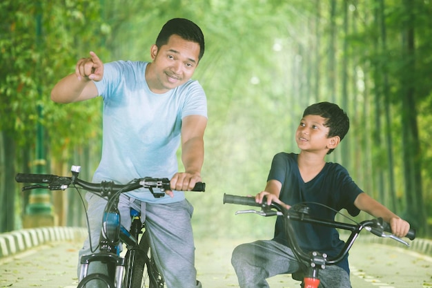 Asiatischer Mann fährt mit seinem Sohn Fahrrad im Park