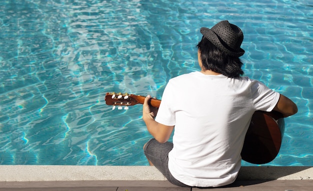 Asiatischer mann gitarre spielen am pool wasser