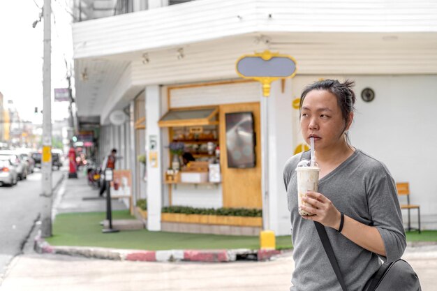 Asiatischer Mann hält den Bubble Ball Ice Milk Tea vor dem Geschäft auf dem Fußweg im Freien