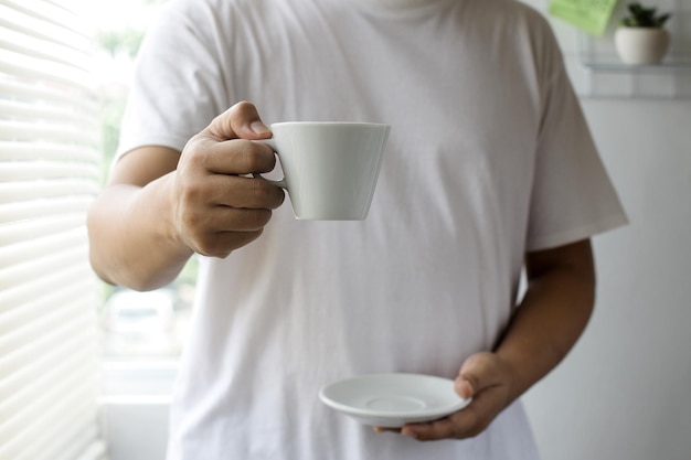 Asiatischer mann im weißen t-shirt, das eine tasse kaffee für modell hält