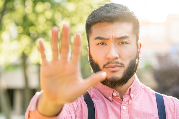 Asiatischer Mann in Freizeitkleidung, der mit der Hand auf Stopp gestikuliert