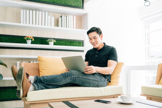 Asiatischer Mann in lässigem Blick auf den Laptop beim Arbeiten und Sitzen auf dem Sofa. Geschäftsmann, der zu Hause mit Problemen an einem Laptop arbeitet. Lösung des Problemprozesses im Geschäft.