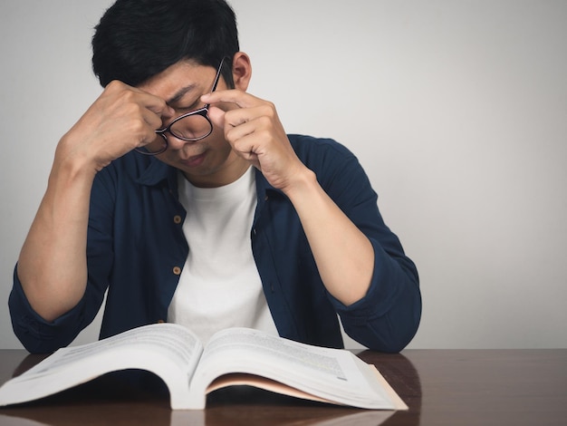 Asiatischer Mann mit Brille versuchte es mit einem Lehrbuch für hartes Lernen auf dem Tisch