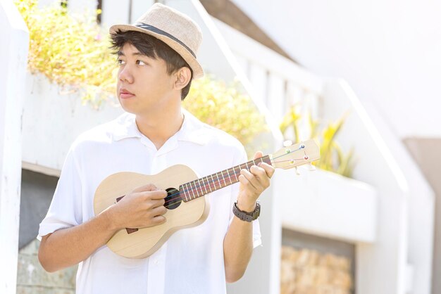 Asiatischer Mann mit Hut, der Gitarren-Ukulele spielt