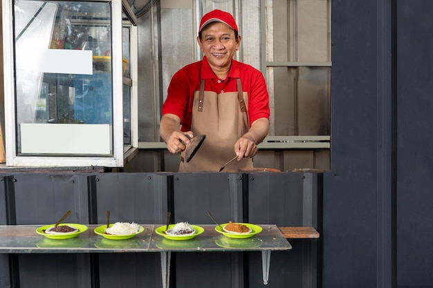 Asiatischer Mann mit Hut und Schürze, der Serabi kocht